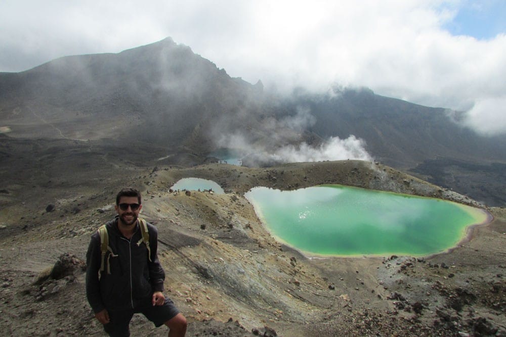 Vivir en Nueva Zelanda chico moreno sonriendo a cámara y detrás un volcán